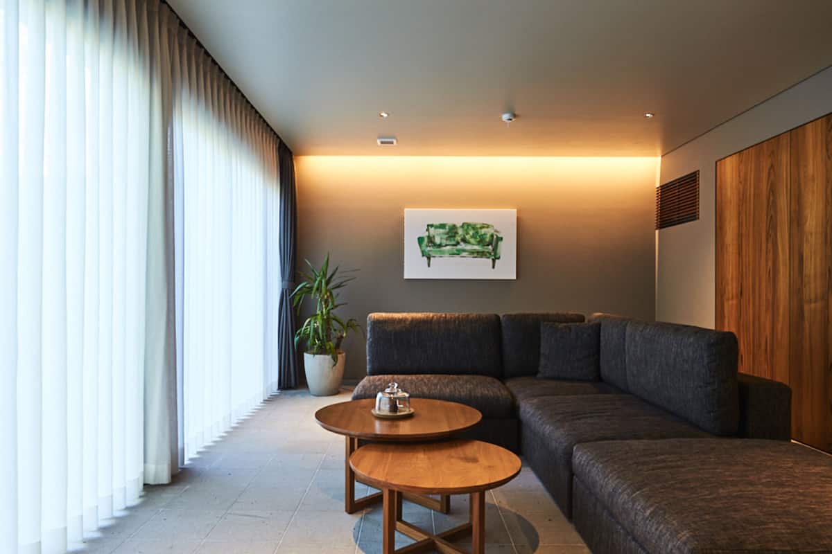 A modern living room with a sectional sofa, two round wooden tables, a potted plant, and a wall-mounted artwork.