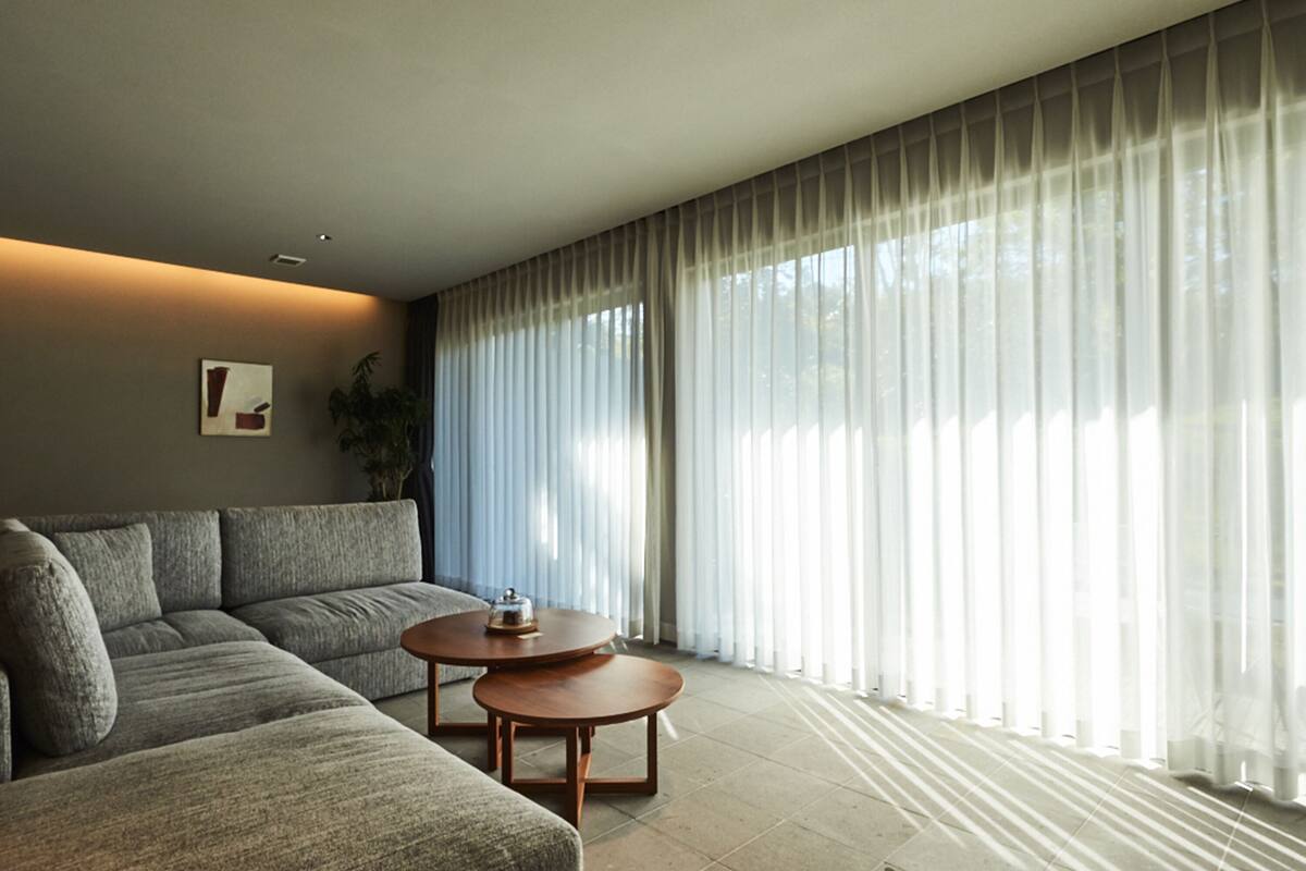 A modern living room with a sectional sofa, two wooden side tables, and sheer curtains.