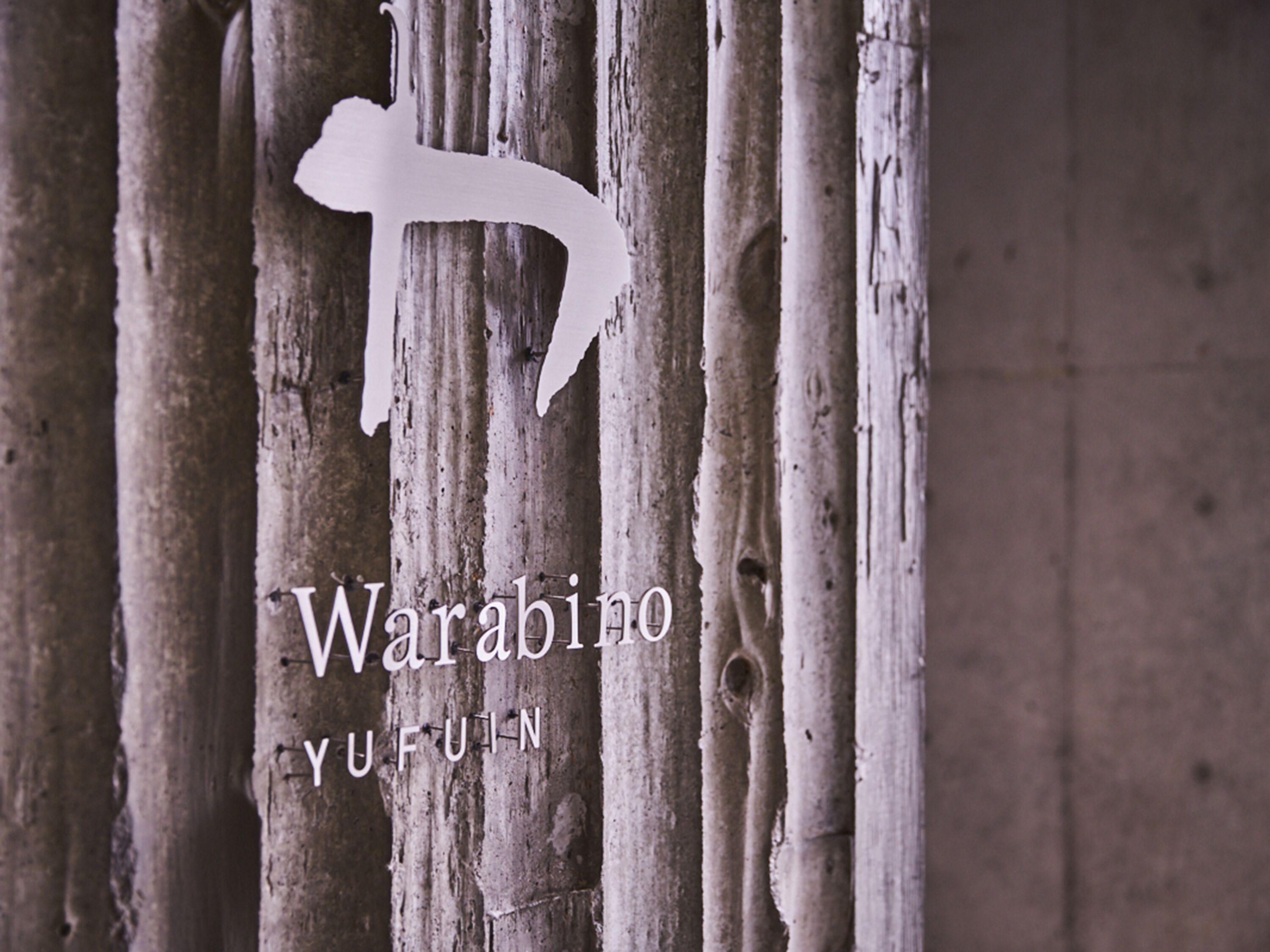 Una estructura de madera con tablones verticales y el contorno blanco de una persona. Se lee el texto 'Warabino YUFUIN'.