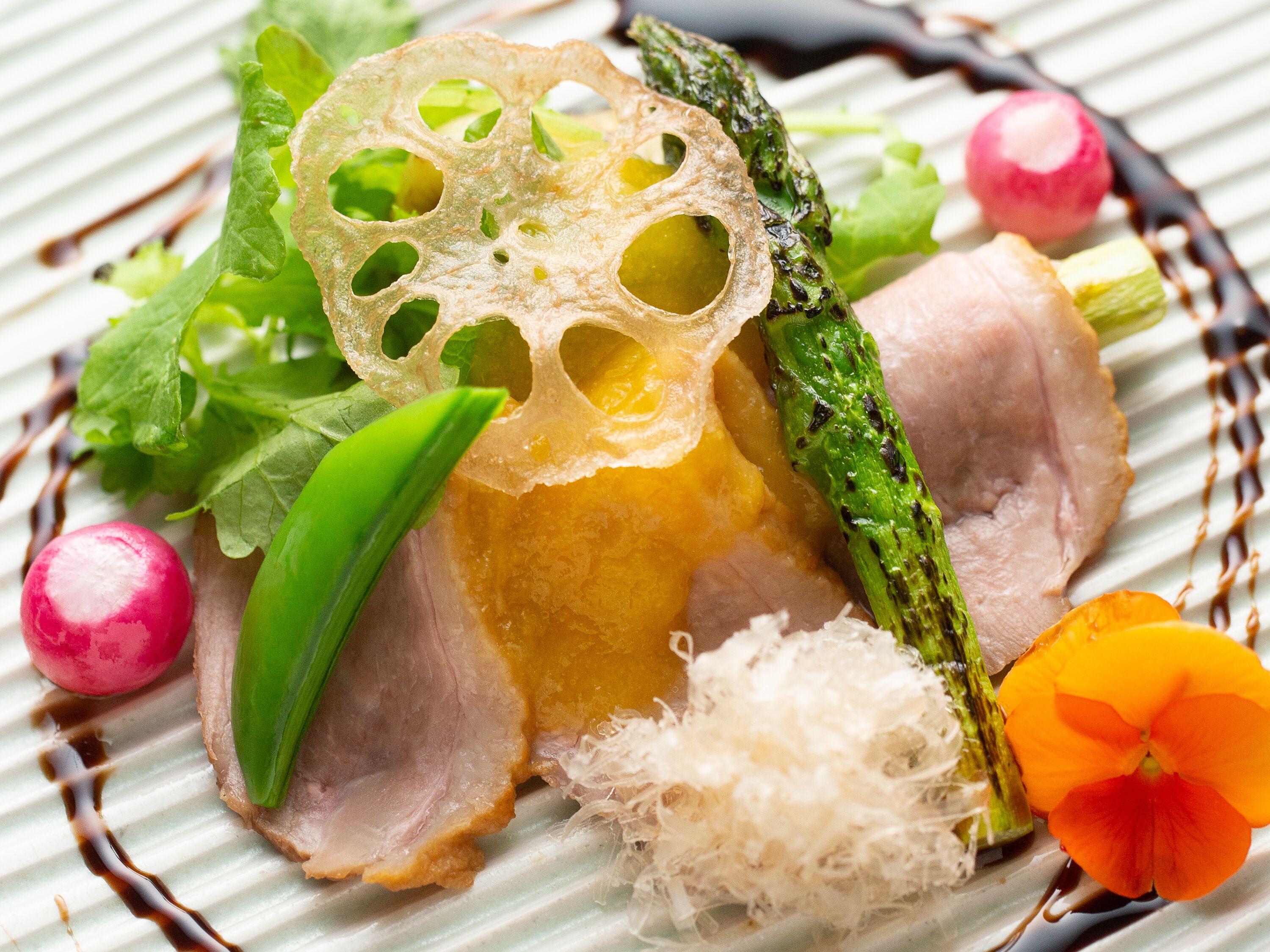 Une assiette contenant une variété de légumes et un morceau de viande, peut-être du porc, garnie de radis daikon râpé et d’une fleur.