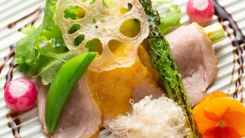 Une assiette contenant une variété de légumes et un morceau de viande, peut-être du porc, garnie de radis daikon râpé et d’une fleur.