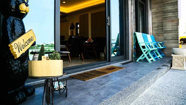 A modern building entrance with a 'Welcome' sign, a patio area with outdoor seating, and a view of the interior. - Mulu-Hotel (Magong)