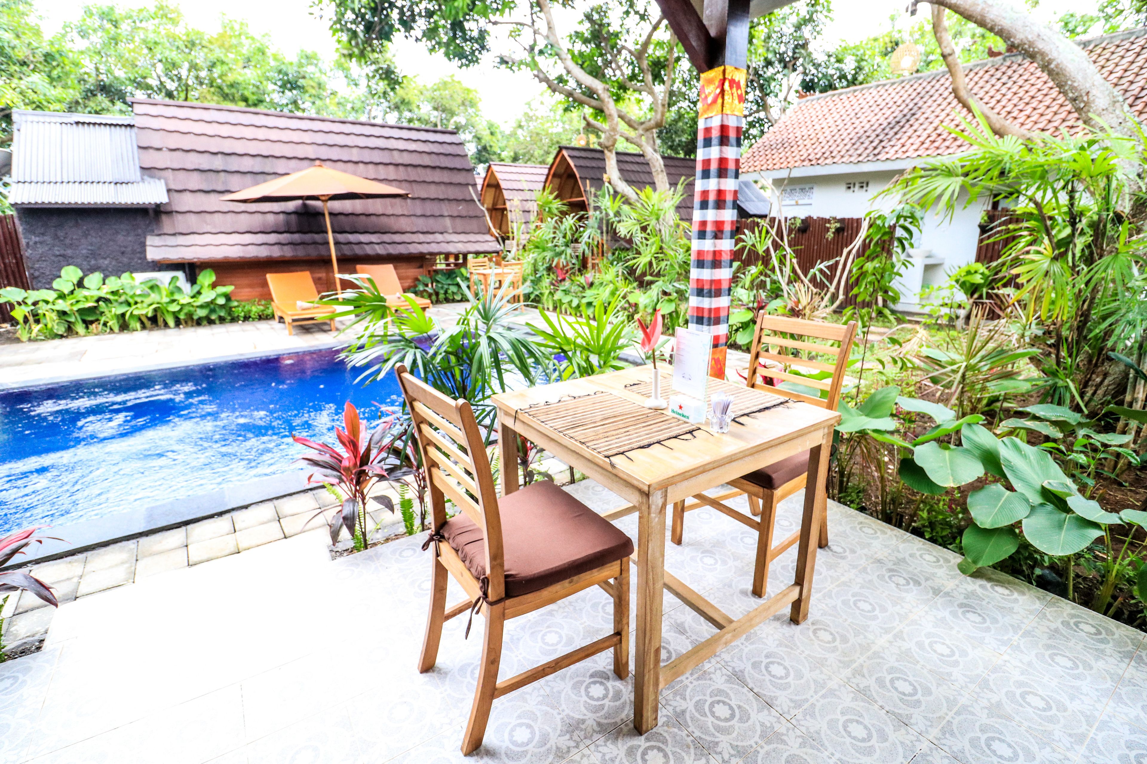 Ein Holztisch und -stühle stehen an einem Pool mit einer gefliesten Terrasse.