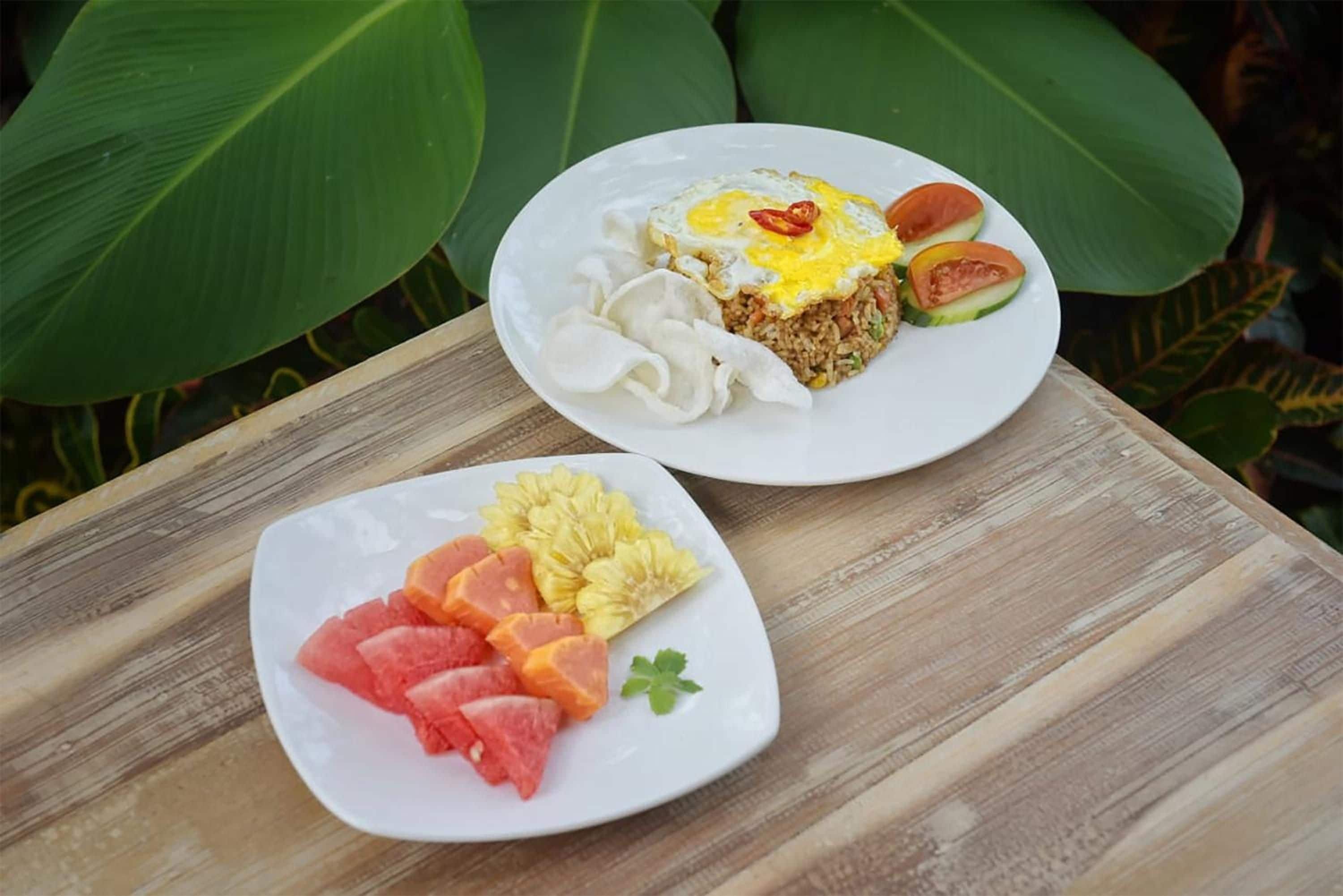 Two plates of food on a wooden table with large green leaves in the background.