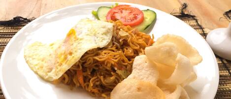 Un plato de comida con fideos, un huevo frito y papas fritas sobre una mesa con un tapete tejido.