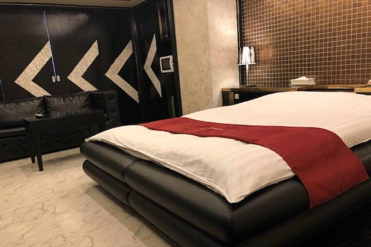A modern bedroom with a large bed, a black sofa, and a decorative wall with geometric patterns.