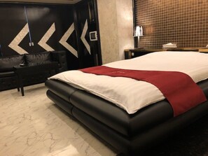 A modern bedroom with a large bed, a black sofa, and a decorative wall with geometric patterns. - Hotel FULULA - Adults Only (Osaka)