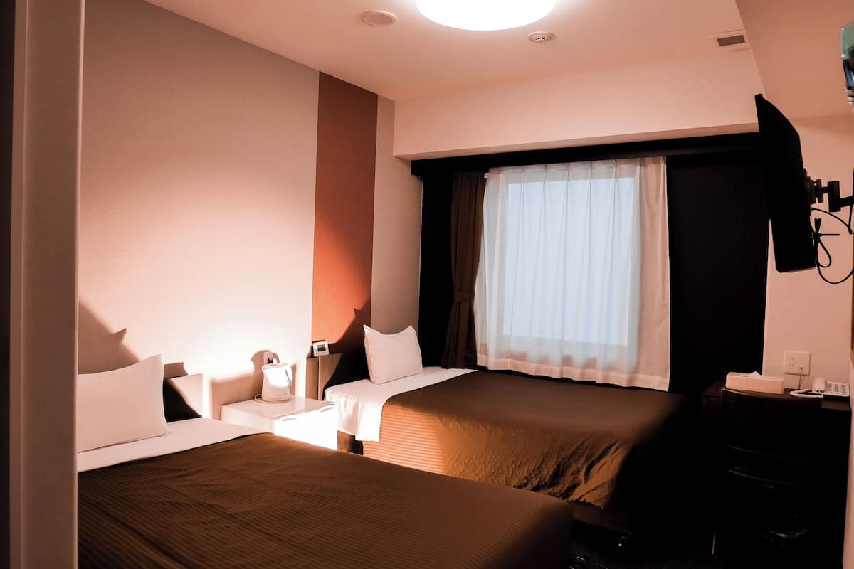 A hotel room with two beds, a desk, a chair, a TV, and a window with curtains.