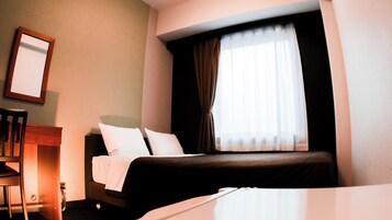 Una habitación de hotel con una cama, una silla, una mesita y un ventanal con cortinas.