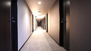 Un couloir d’hôtel avec des revêtements de sol en moquette, des portes des deux côtés et des luminaires encastrés au plafond.