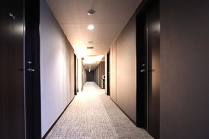 Pasillo de hotel con piso alfombrado, puertas a ambos lados e iluminación empotrada en el techo.