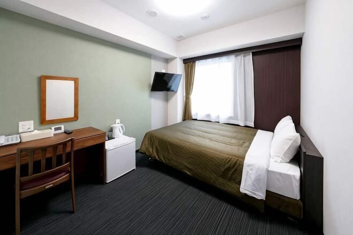 A hotel room with a bed, a desk, a chair, a television, and a window with curtains.