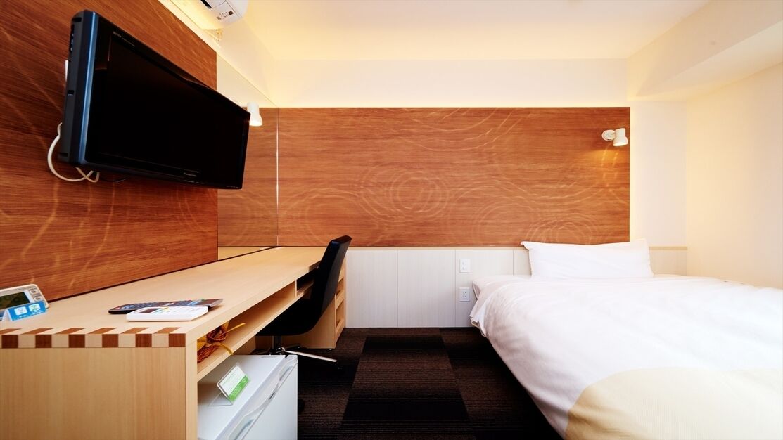 Een hotelkamer met een bed, een bureau met stoel, een aan de muur bevestigde televisie en een houten accentmuur.