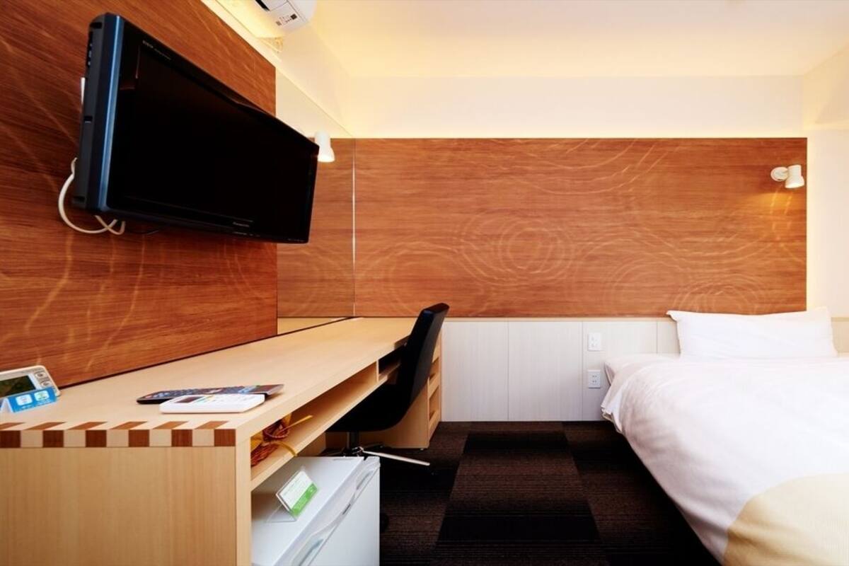 Ein Hotelzimmer mit Bett, Schreibtisch mit Stuhl, einem an der Wand befestigten Fernseher und einer Holzvertäfelung.