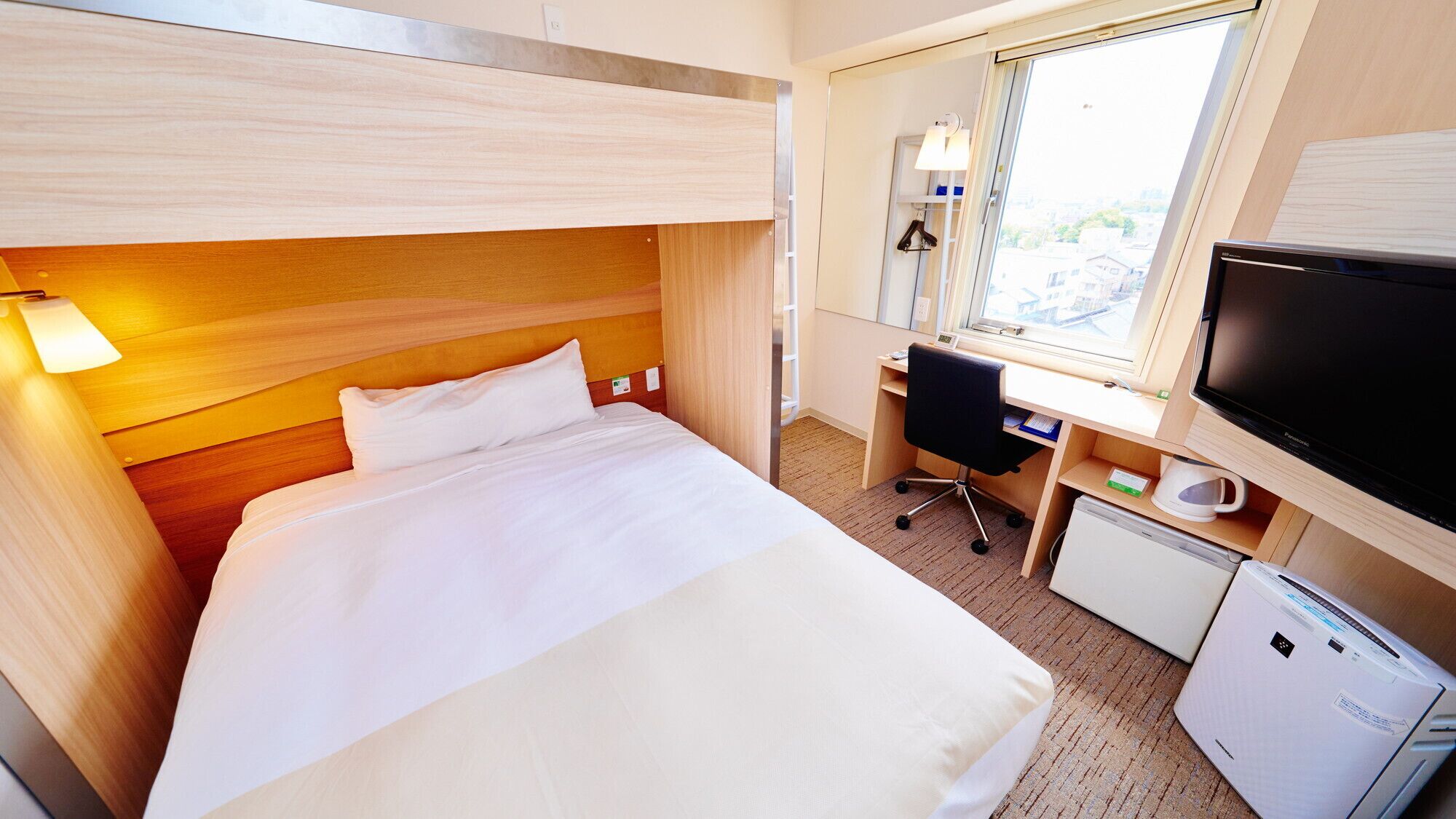 Een hotelkamer met een stapelbed, een bureau met een computer, een televisie en een minibar.