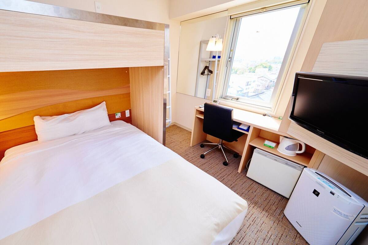 Ein Hotelzimmer mit Etagenbett, Schreibtisch, Computer, Fernseher und Minikühlschrank.