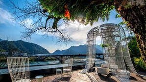 A wooden deck with metal chairs and a small table, overlooking a river and mountains. - Dreamhouse (Hangzhou)