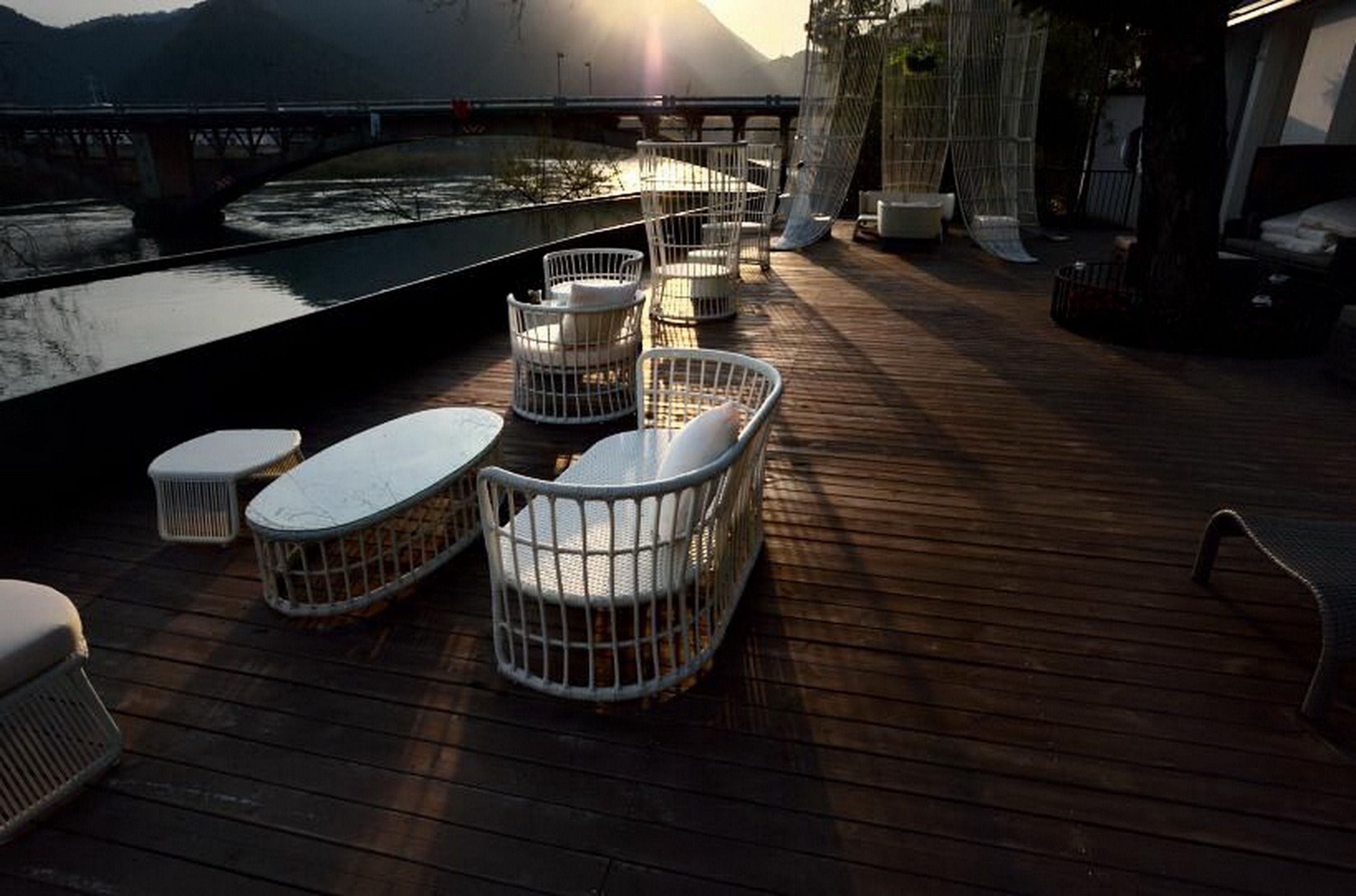 A deck with outdoor seating, a view of a river, and a bridge in the background.