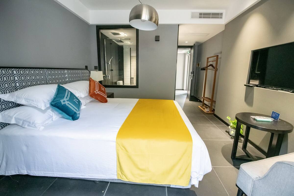 A hotel room with a bed, a TV, a bedside table, and a mirror.