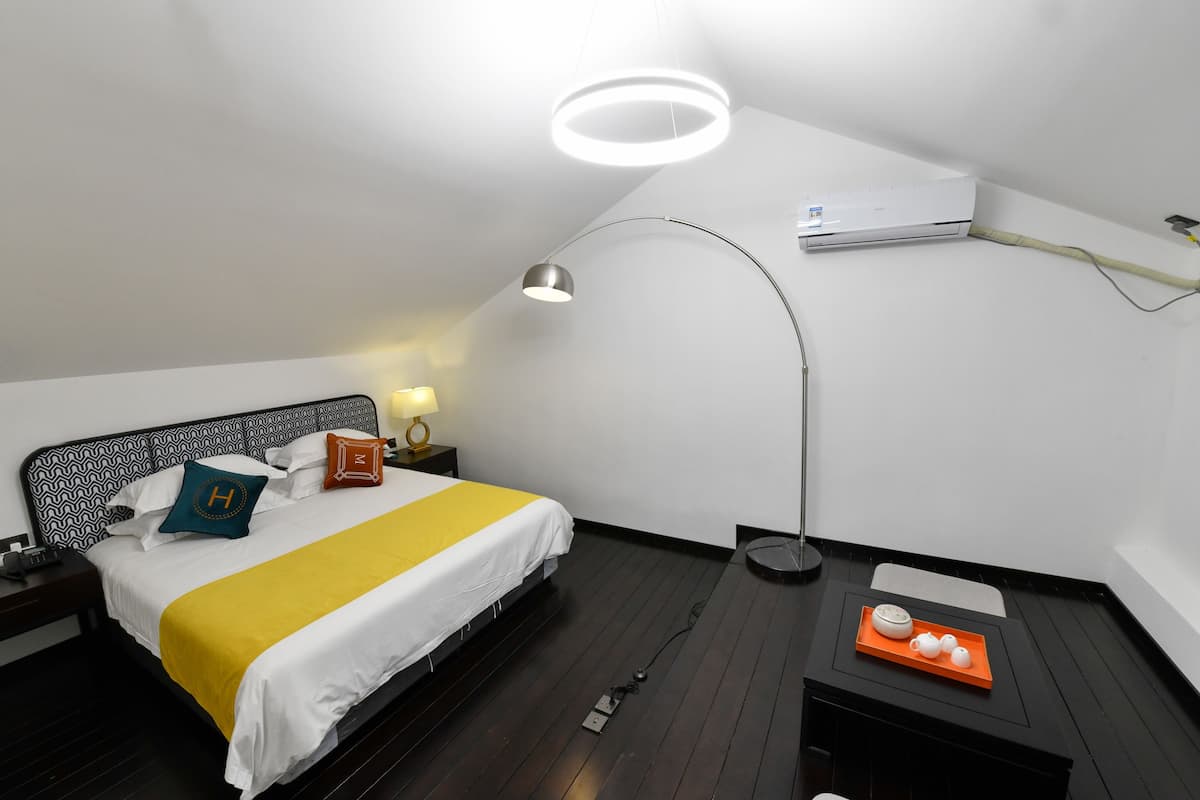 A modern hotel room with a bed, bedside table, lamp, air conditioning unit, and a tray with teapots.