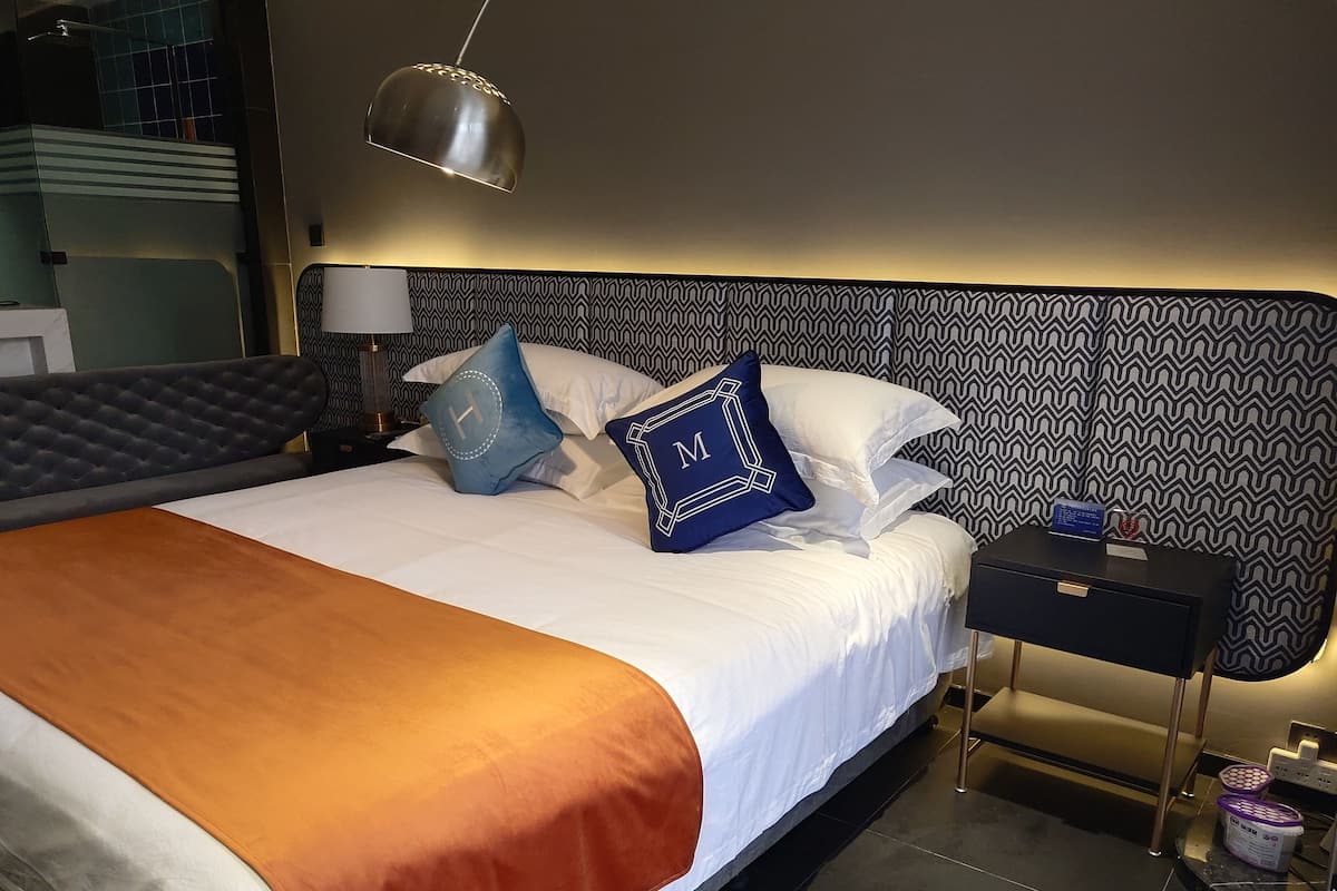 A hotel room with a bed, a nightstand, a lamp, and a wall with a geometric pattern.