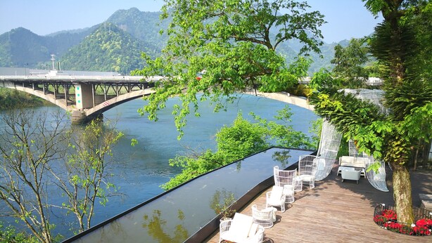 A riverside deck with outdoor seating and a view of a bridge and mountains. - Dreamhouse (Hangzhou)