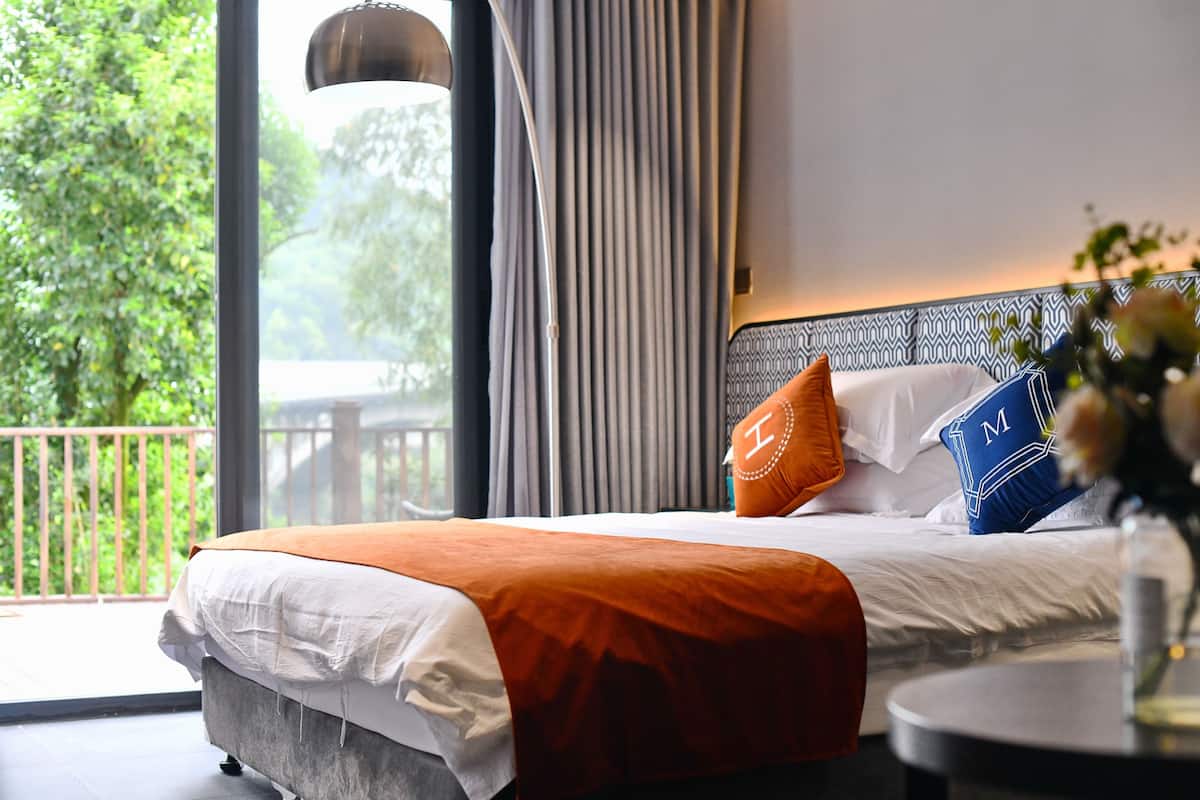 A hotel room with a bed, a round table, and a view of greenery outside.