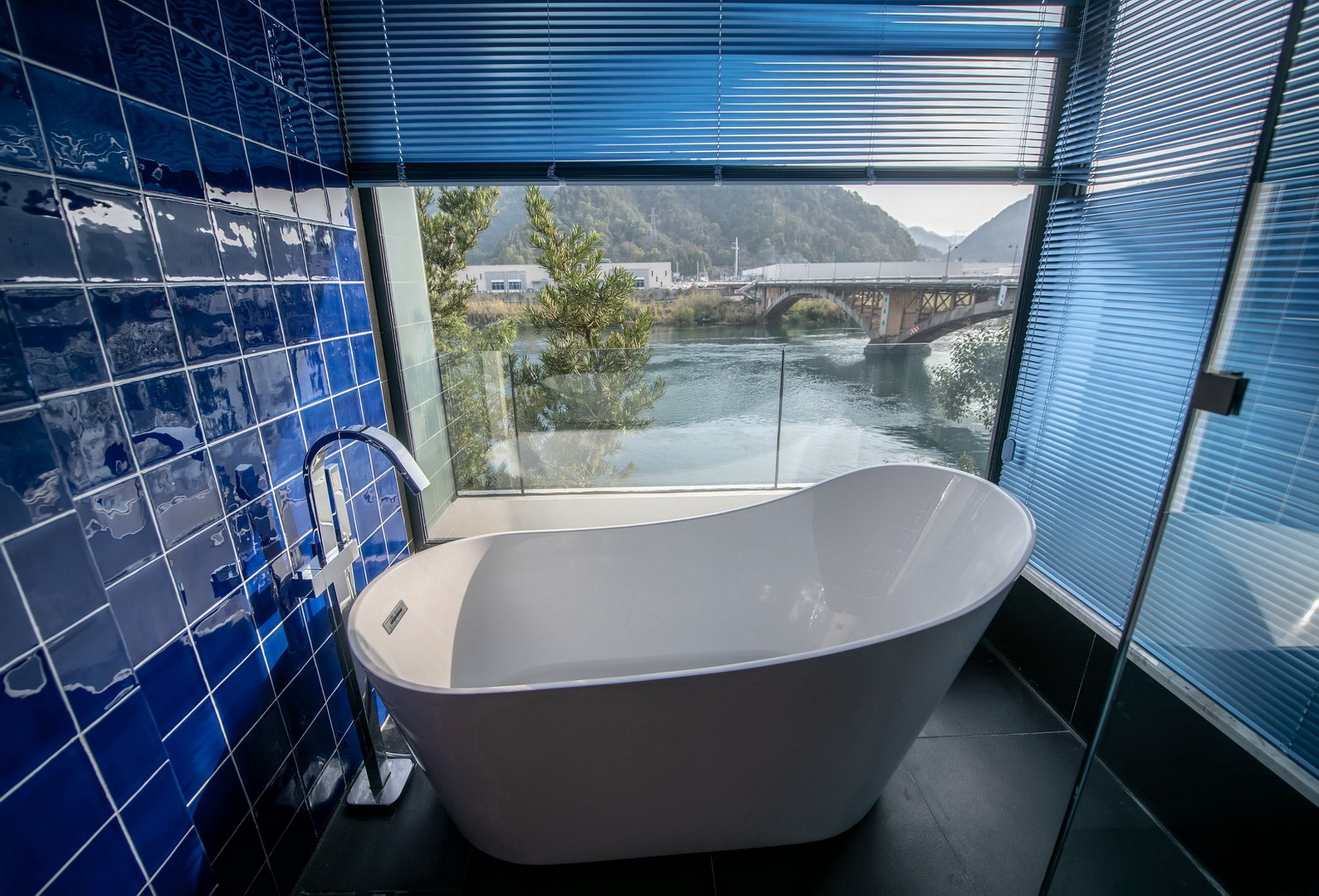 A modern bathroom with a freestanding bathtub, large windows, and a view of a bridge over a river.