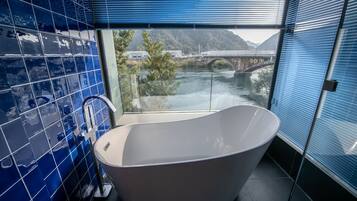 A modern bathroom with a freestanding bathtub, large windows, and a view of a bridge over a river.