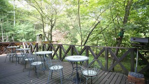 A wooden deck with metal tables and chairs, surrounded by trees. - Piccolo Hotel Opera Karuizawa (Karuizawa)