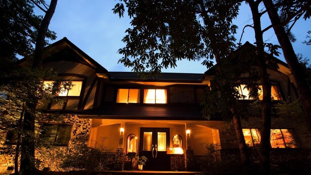 A two-story house with a stone facade, multiple windows, and a front porch with steps leading to the entrance. - Piccolo Hotel Opera Karuizawa (Karuizawa)