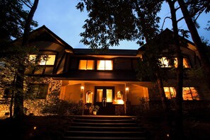 A two-story house with a stone facade, multiple windows, and a front porch with steps leading to the entrance.