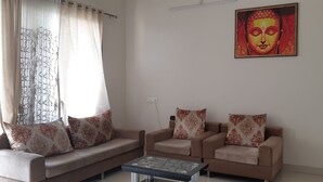 A living room with two sofas and a coffee table, a Buddha painting on the wall, and a power outlet. - Arista Service Apartments Ghansoli (Navi Mumbai)
