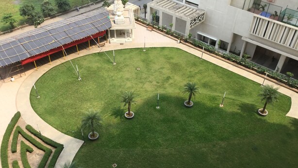A courtyard with a central lawn, palm trees, and a small temple-like structure. - Arista Service Apartments Ghansoli (Navi Mumbai)