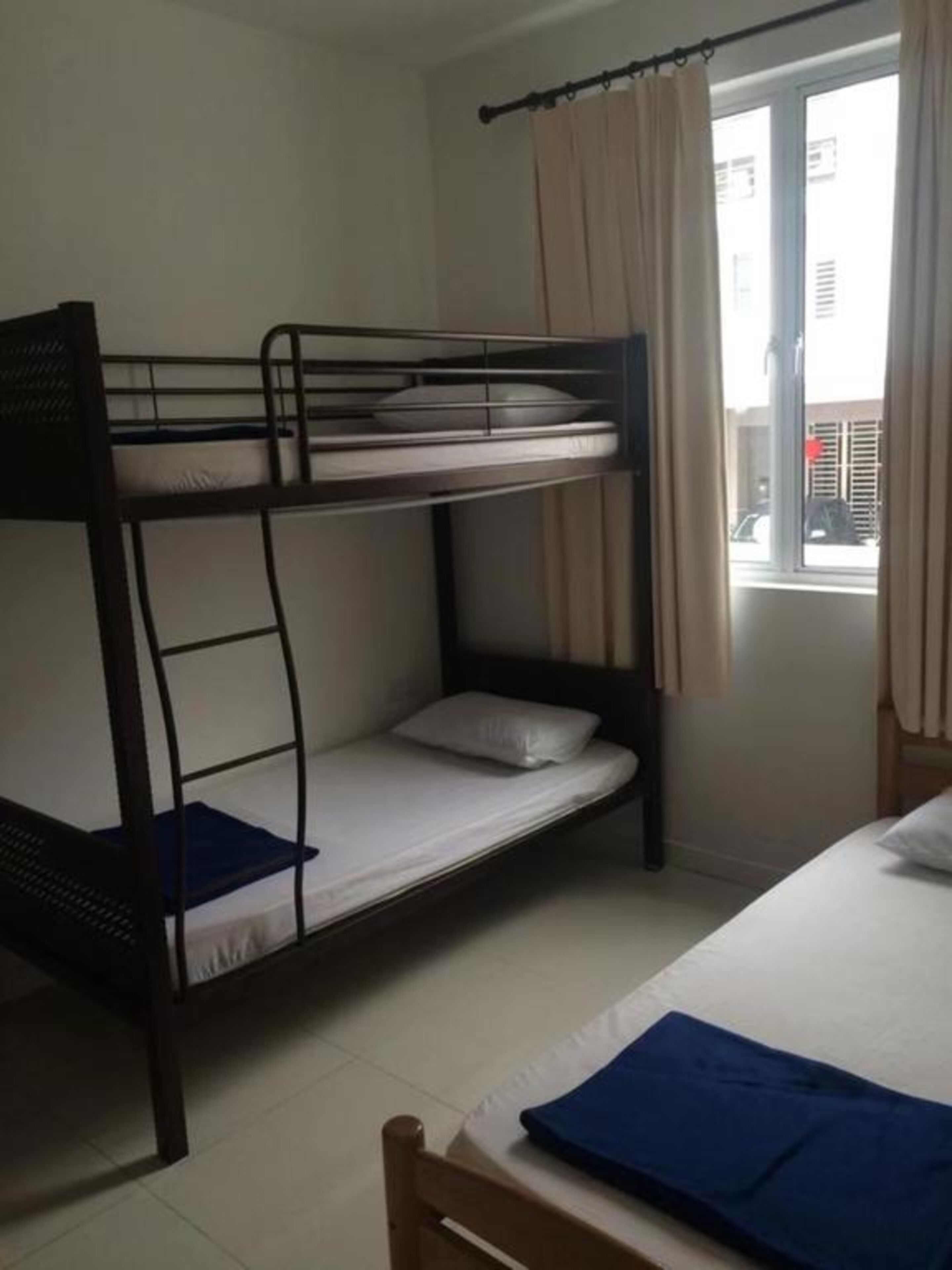 A bunk bed room with a window, curtains, and a view of buildings outside.