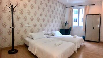 Een hotelkamer met twee bedden, een kapstok, een bureau, een stoel en een deur.