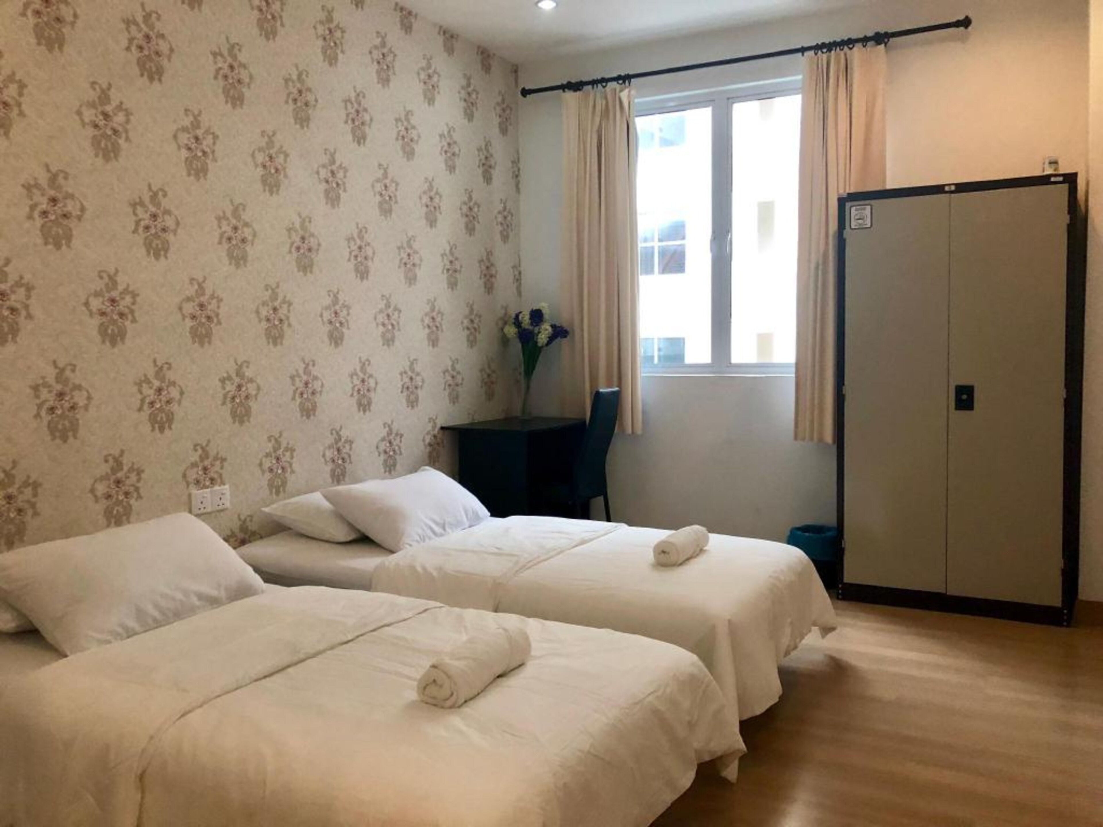 Een hotelkamer met twee bedden, een bureau, een stoel, een raam met gordijnen en een kledingkast.