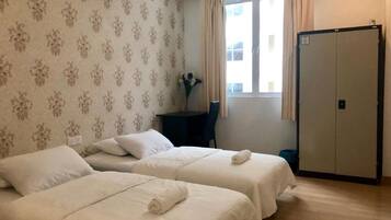 Een hotelkamer met twee bedden, een bureau, een stoel, een raam met gordijnen en een kledingkast.