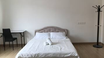 Een net opgemaakt bed met een geborduurde hoofdbord, een klein tafeltje met een stoel en een kapstok.