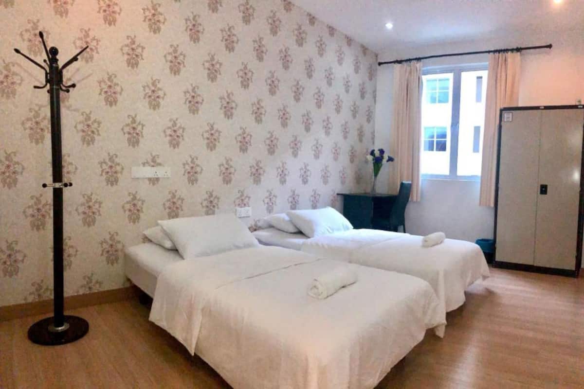 Camera d'albergo con due letti, un appendiabiti, una scrivania con sedia e una finestra con tende.