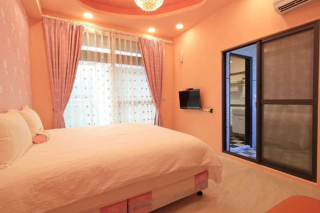 A bedroom with a bed, curtains, a television, and a view of the bathroom through a sliding door.