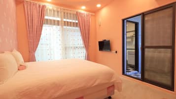 A bedroom with a bed, curtains, a television, and a view of the bathroom through a sliding door.