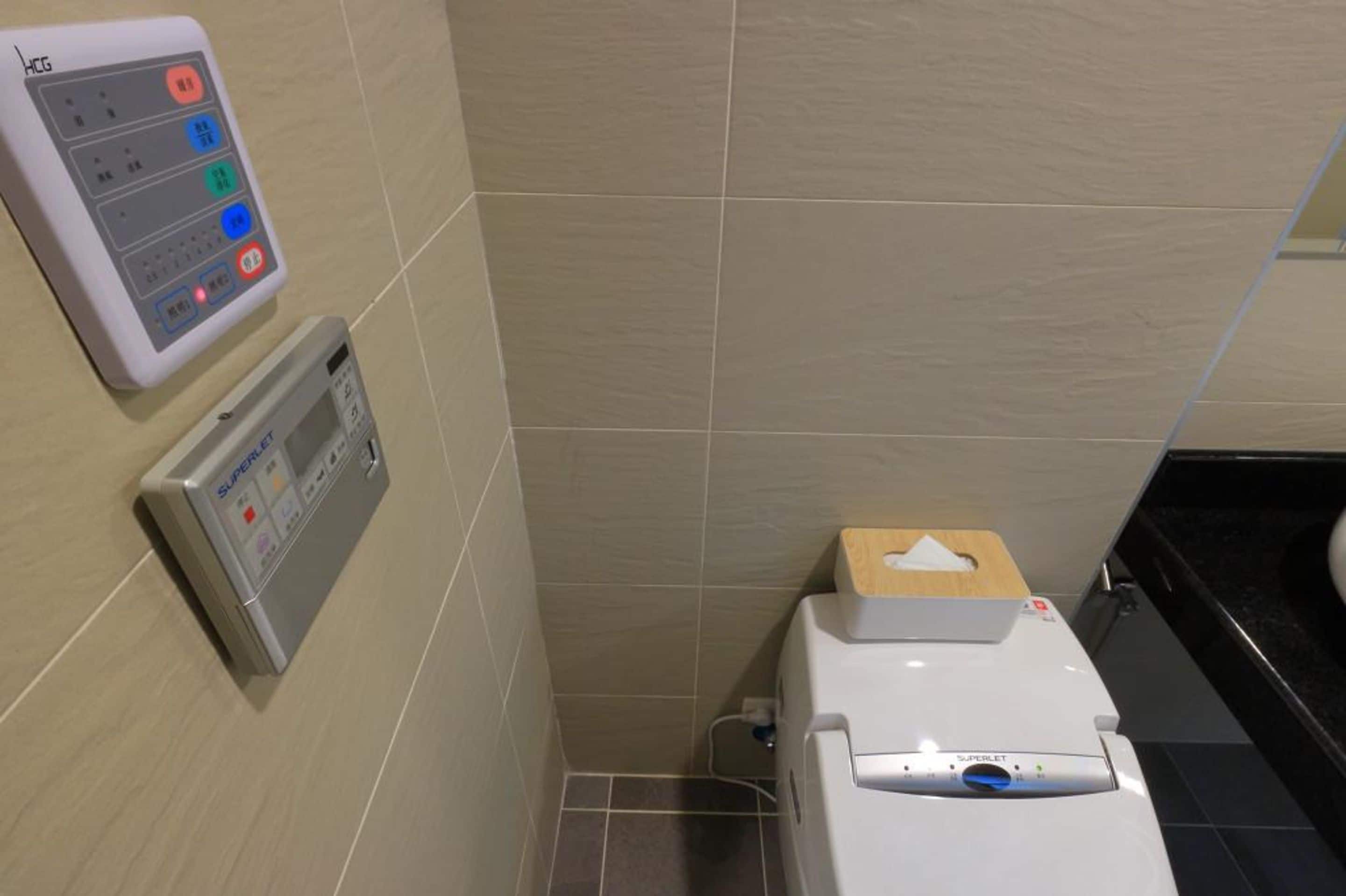 Un baño con inodoro, secamanos y panel de control en la pared.