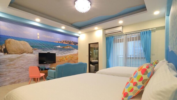 Ein Hotelzimmer mit Bett, Schreibtisch, Stuhl, Fernseher und einem Wandbild mit Strandmotiv.