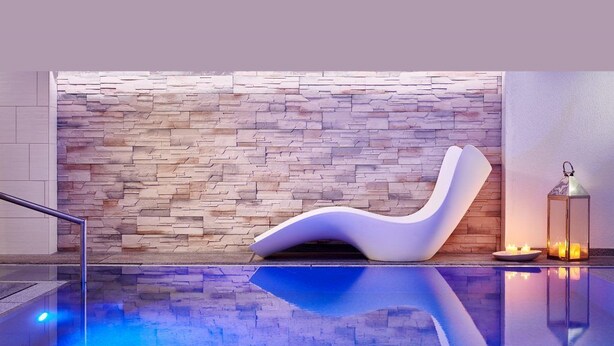 Ein moderner Entspannungsbereich mit einer Steinwand, einem weißen Lounge-Sessel und einem Spiegelteich.