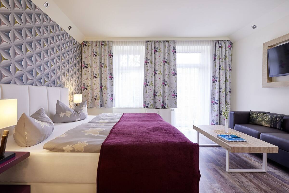 Une chambre d’hôtel comprenant un lit, une table basse en bois, un canapé et un panneau décoratif mural.