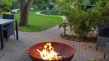 Un hogar de fuego en un jardín con suelo de ladrillo y vegetación circundante.