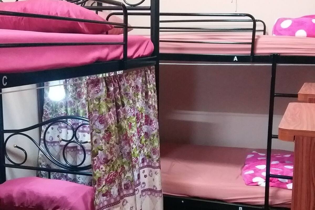 Een slaapzaal met stapelbedden, een ventilator en een raam.