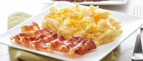 A plate of scrambled eggs with cheese and bacon on a white plate.