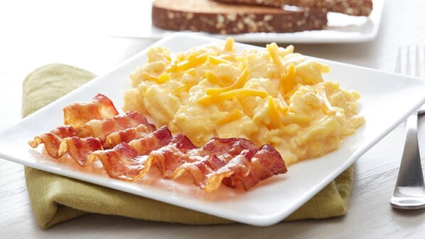 Un plato de huevos revueltos con queso y tocino sobre un plato blanco.